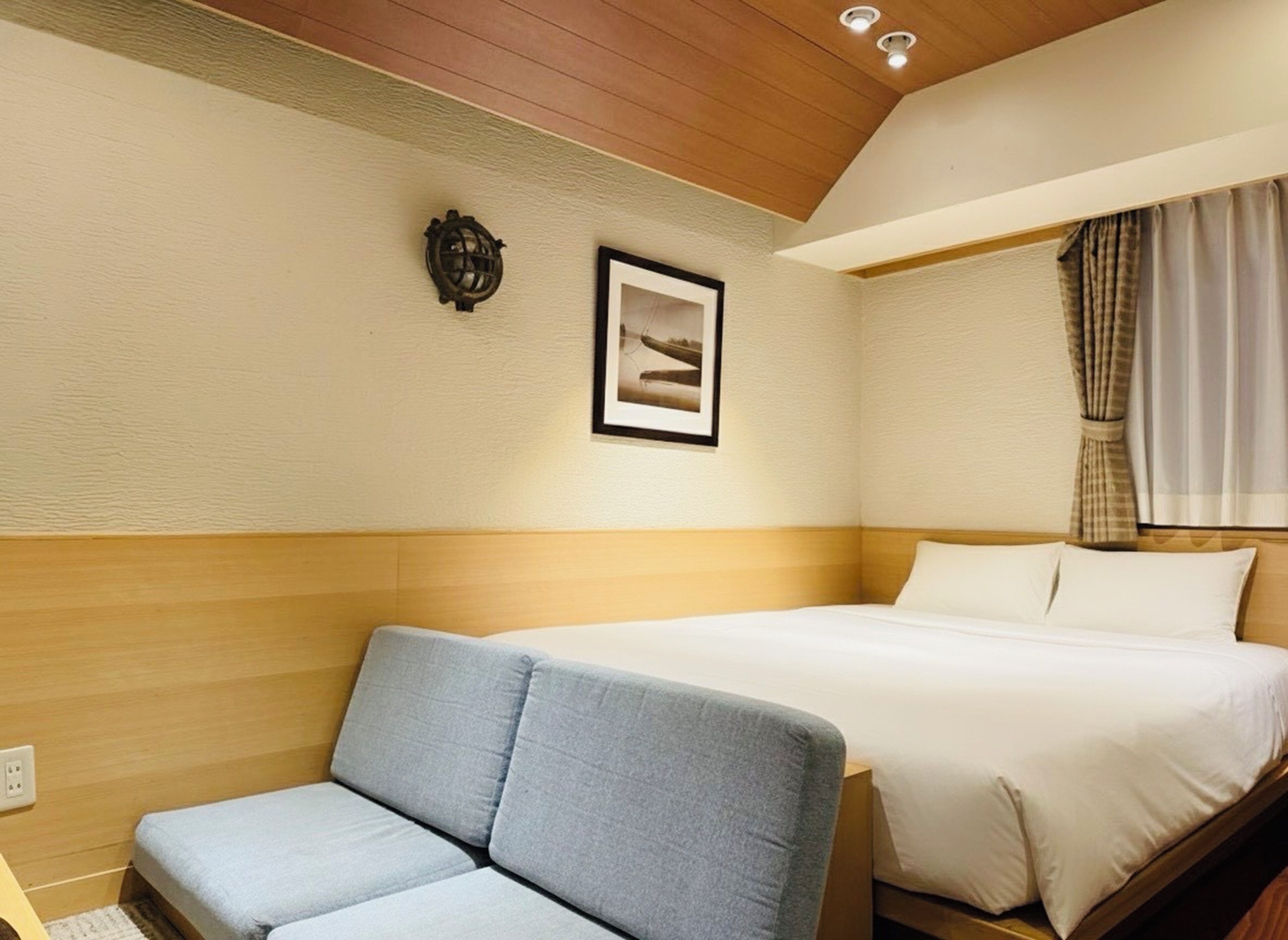 Een hotelkamer met een bed, een bank, een aan de muur hangend schilderij en een plafondlamp.