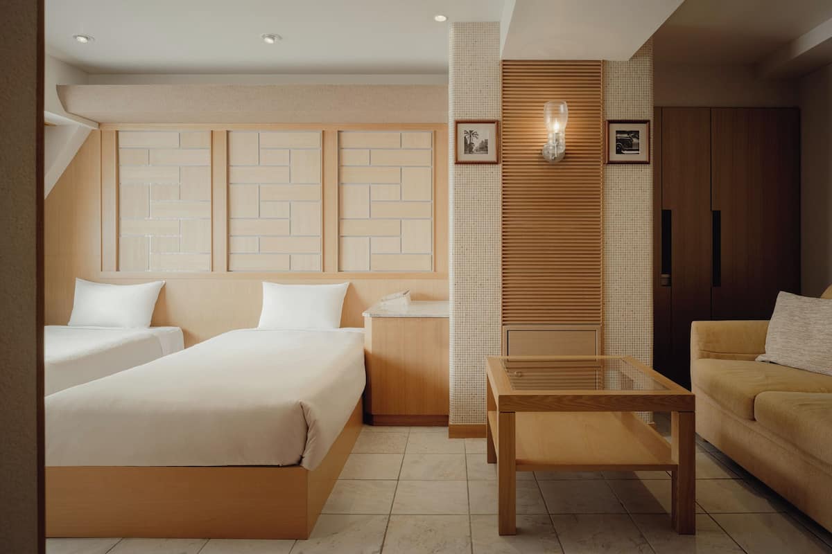 A hotel room with two beds, a sofa, a small table, and a cabinet.