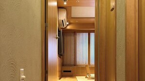 A narrow hallway with wooden flooring, a small seating area with a bench, and a window with vertical blinds. - Nest Hotel Olt Kawasaki Station (Kawasaki)