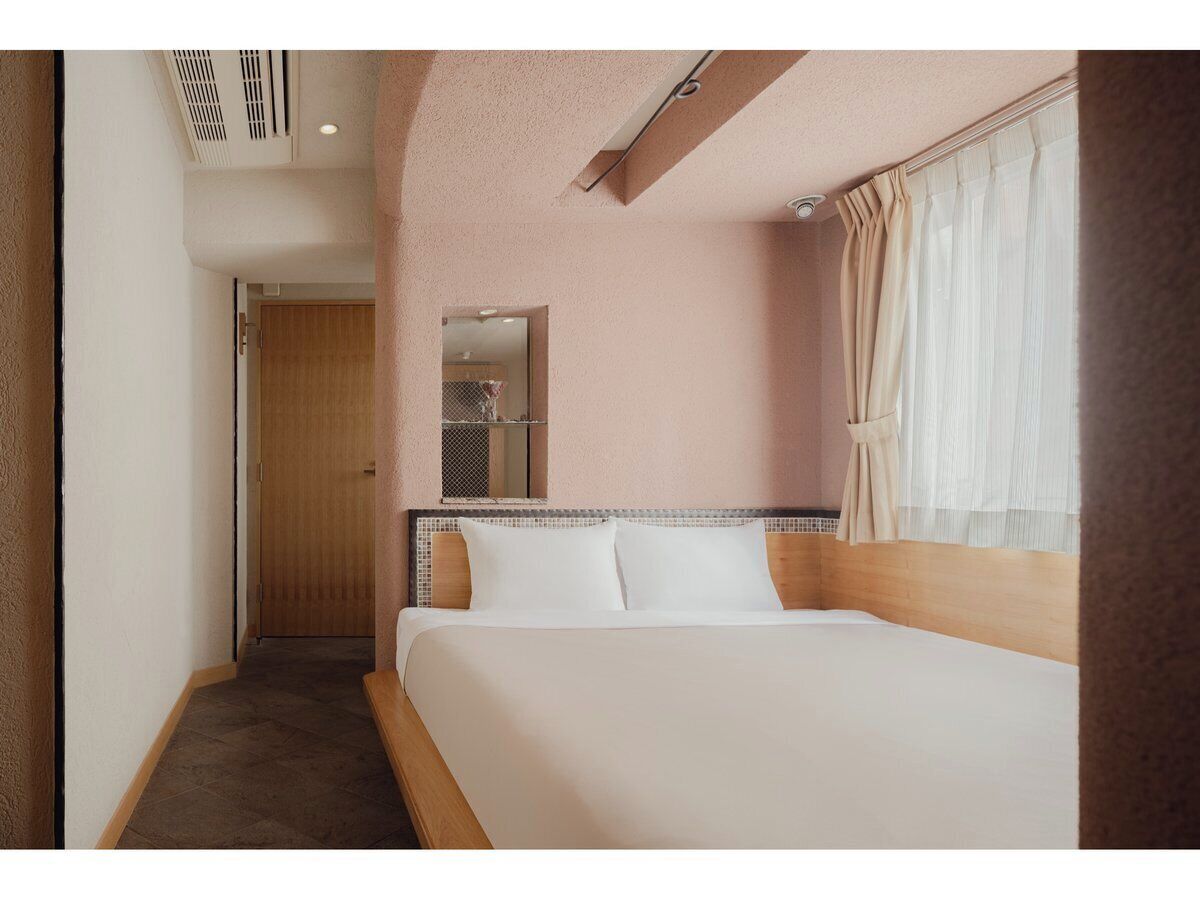 Habitación de hotel con cama, cabecera de madera, espejo y ventana con cortinas.