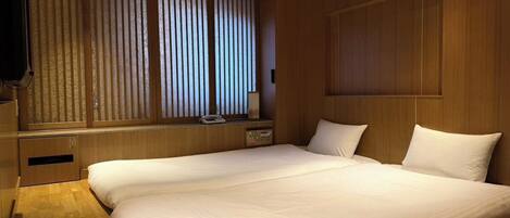 Habitación de hotel con una cama grande, paneles de madera, una ventana con persianas y una mesita de noche con lámpara.