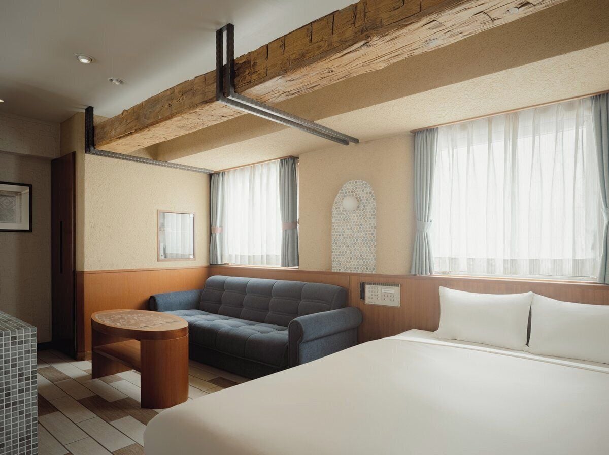 A hotel room with a bed, a sofa, a small round table, and a window with curtains.