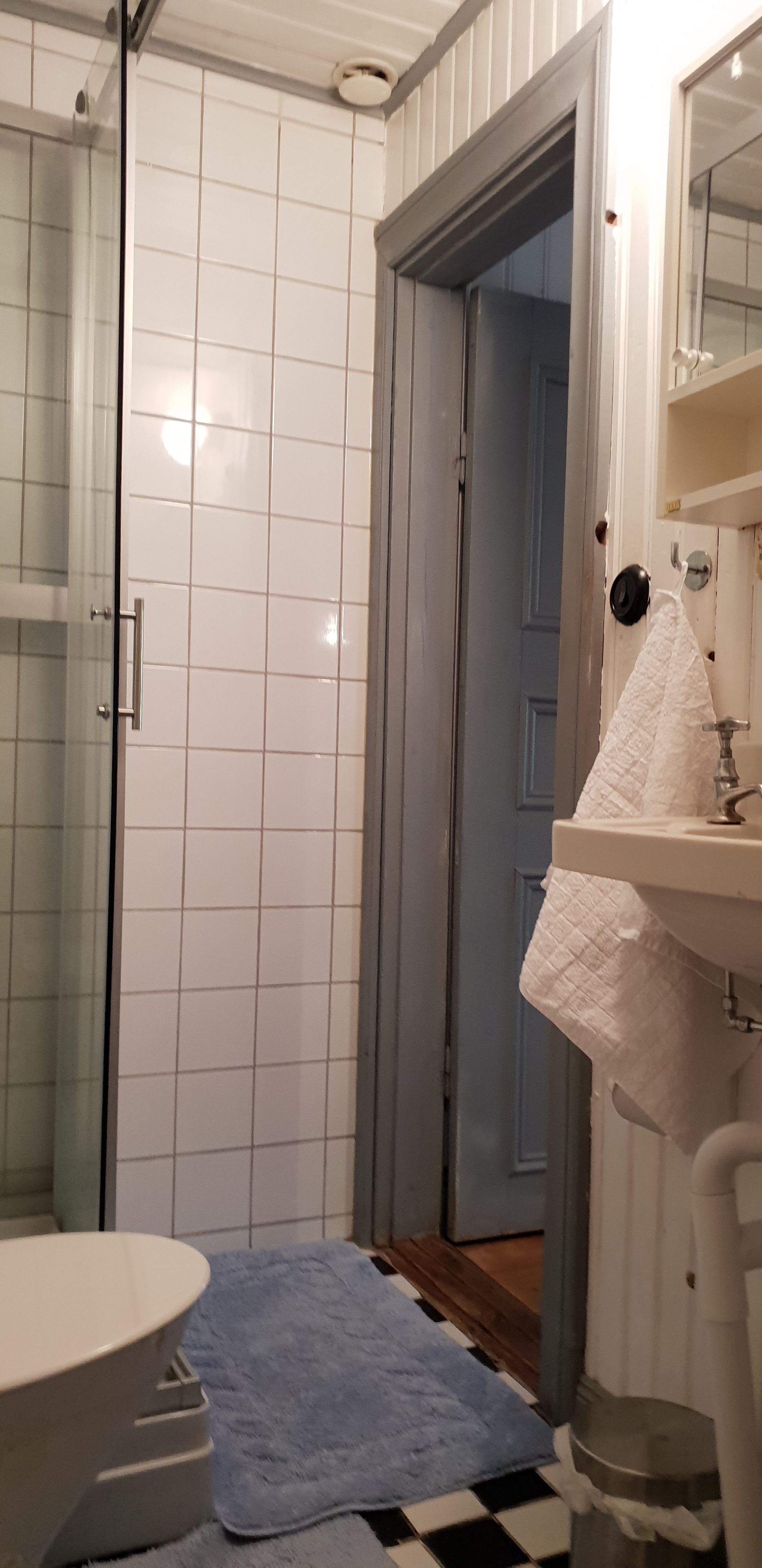 A bathroom with a glass shower enclosure, a sink with a white towel, and a blue bath mat on a checkered floor.