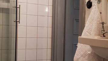 A bathroom with a glass shower enclosure, a sink with a white towel, and a blue bath mat on a checkered floor.