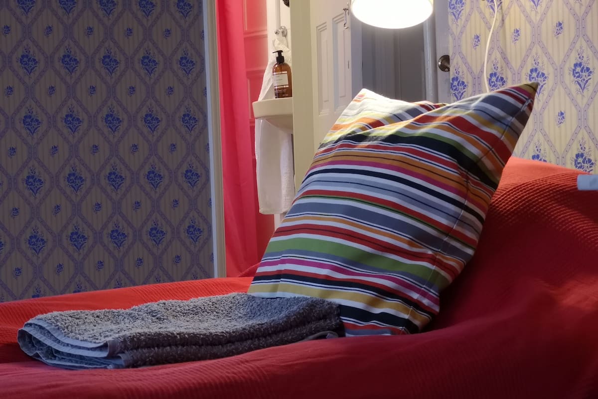 Ein Zimmer mit einem roten Sofa, einem gestreiften Kissen und einer Wand mit Muster.