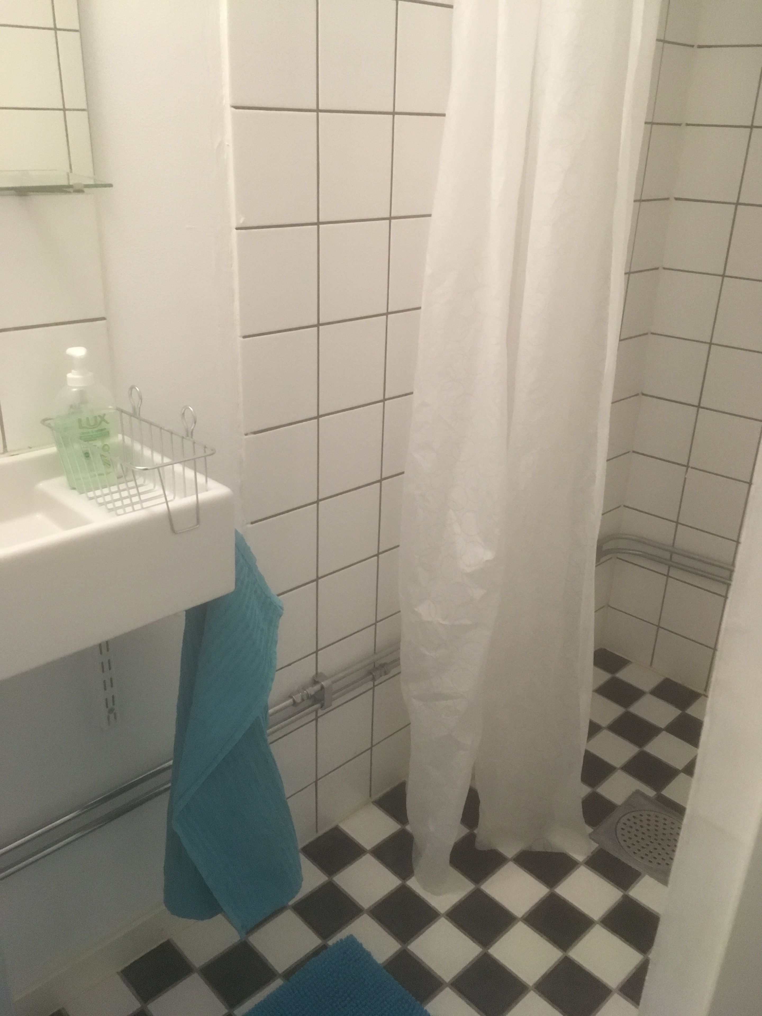 Un baño con un lavabo blanco, un espejo, una cortina de ducha y un suelo a cuadros.