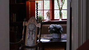 Una habitación con una silla de madera, una mesa con un jarrón y una estantería.
