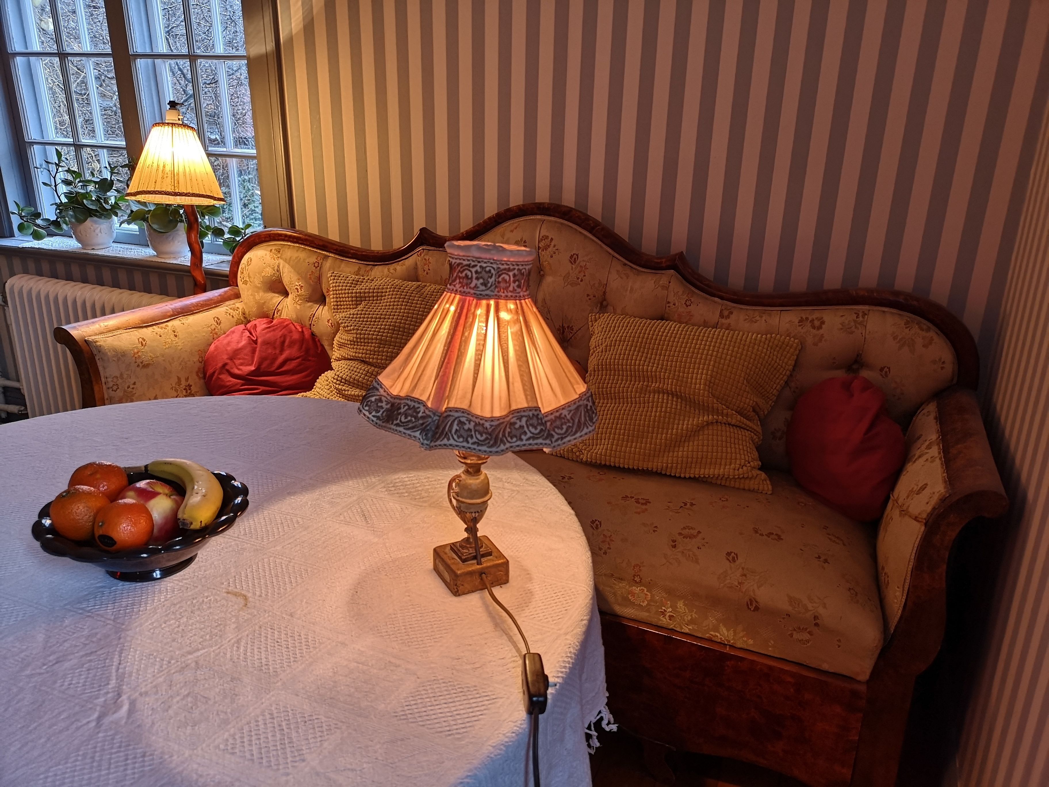 A cozy room with a round table, a lamp, and a fruit bowl.