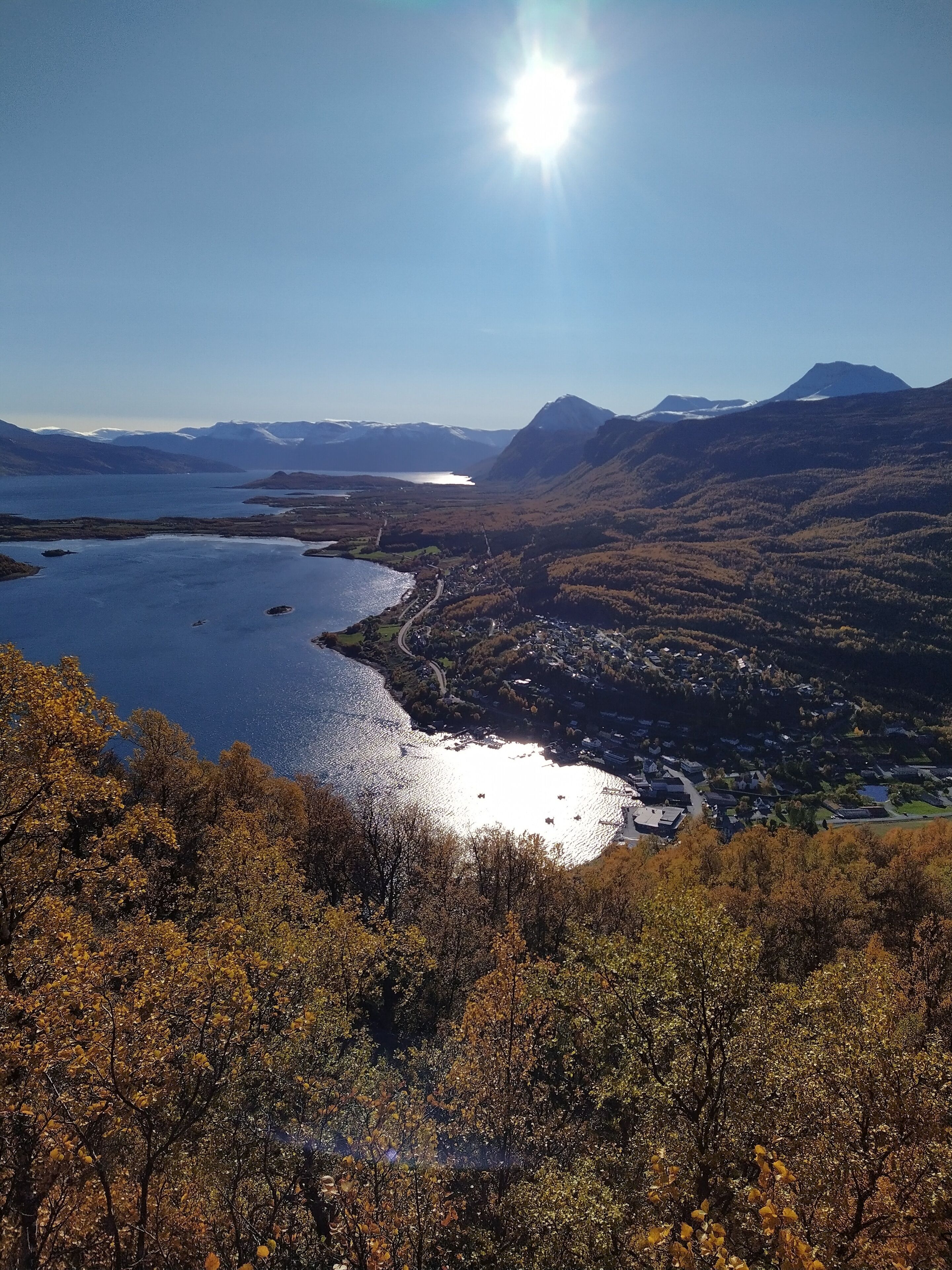 Weitläufige Aussicht auf eine Berglandschaft mit einem See, einer kleinen Stadt und wolkenlosem Himmel.