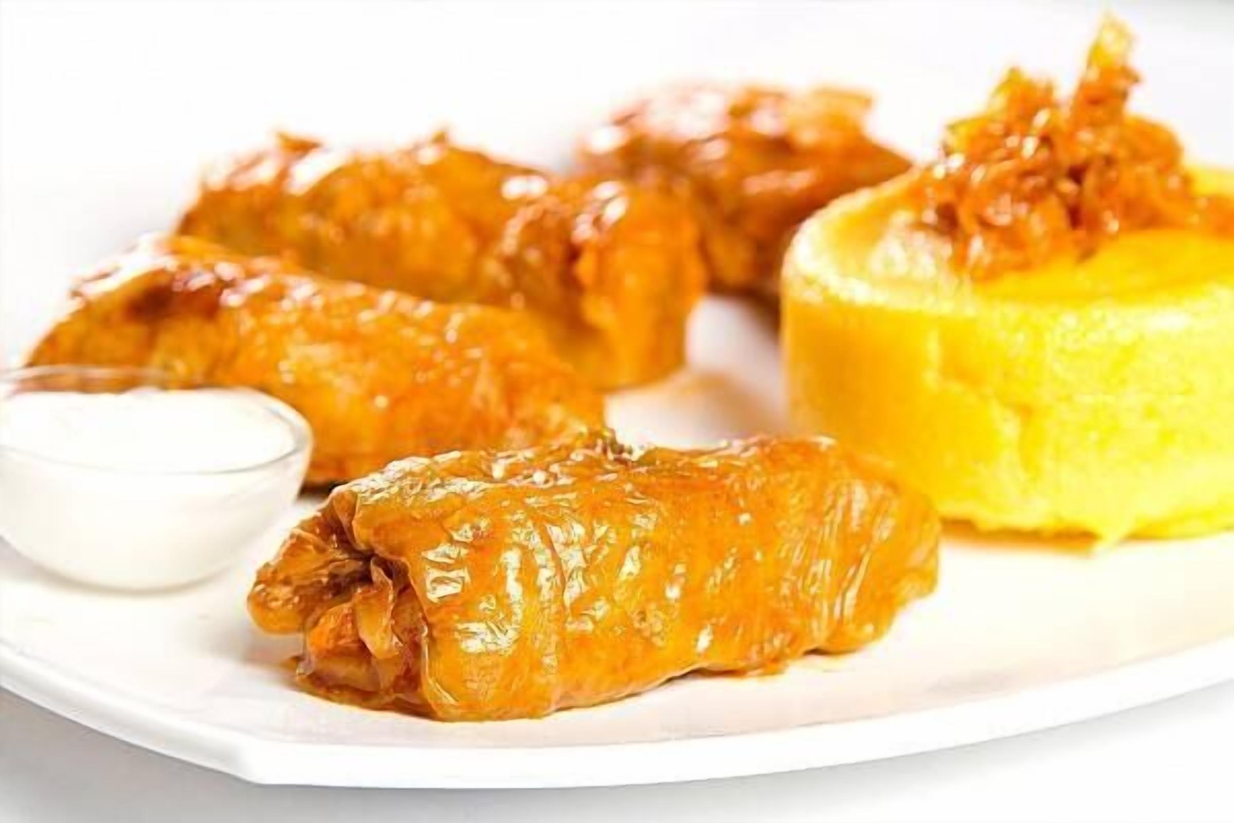 Un plato de rollos de col rellenos, acompañados de salsa y un cuenco pequeño de salsa blanca.