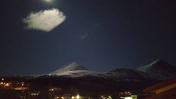 A mountain with a snow-capped peak under a night sky with a visible moon and a cloud.