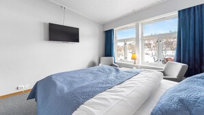 Een hotelkamer met twee bedden, een aan de muur bevestigde televisie, een raam met gordijnen en een stoel.