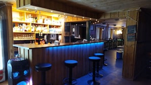 Een bar met een houten toonbank, krukken en gevulde flessenrekken.