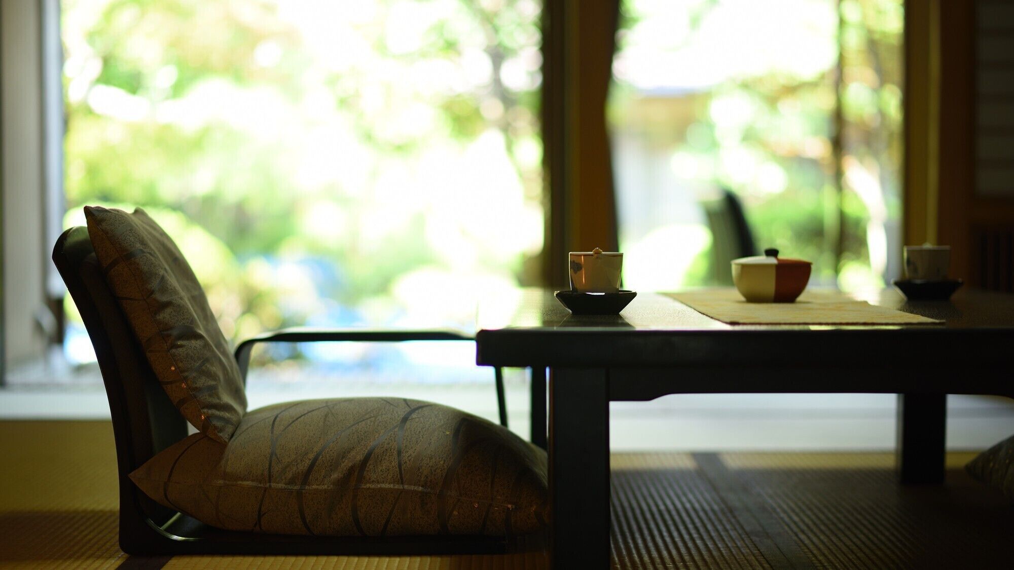 A room with a chair, a table, and a window with a view of greenery.