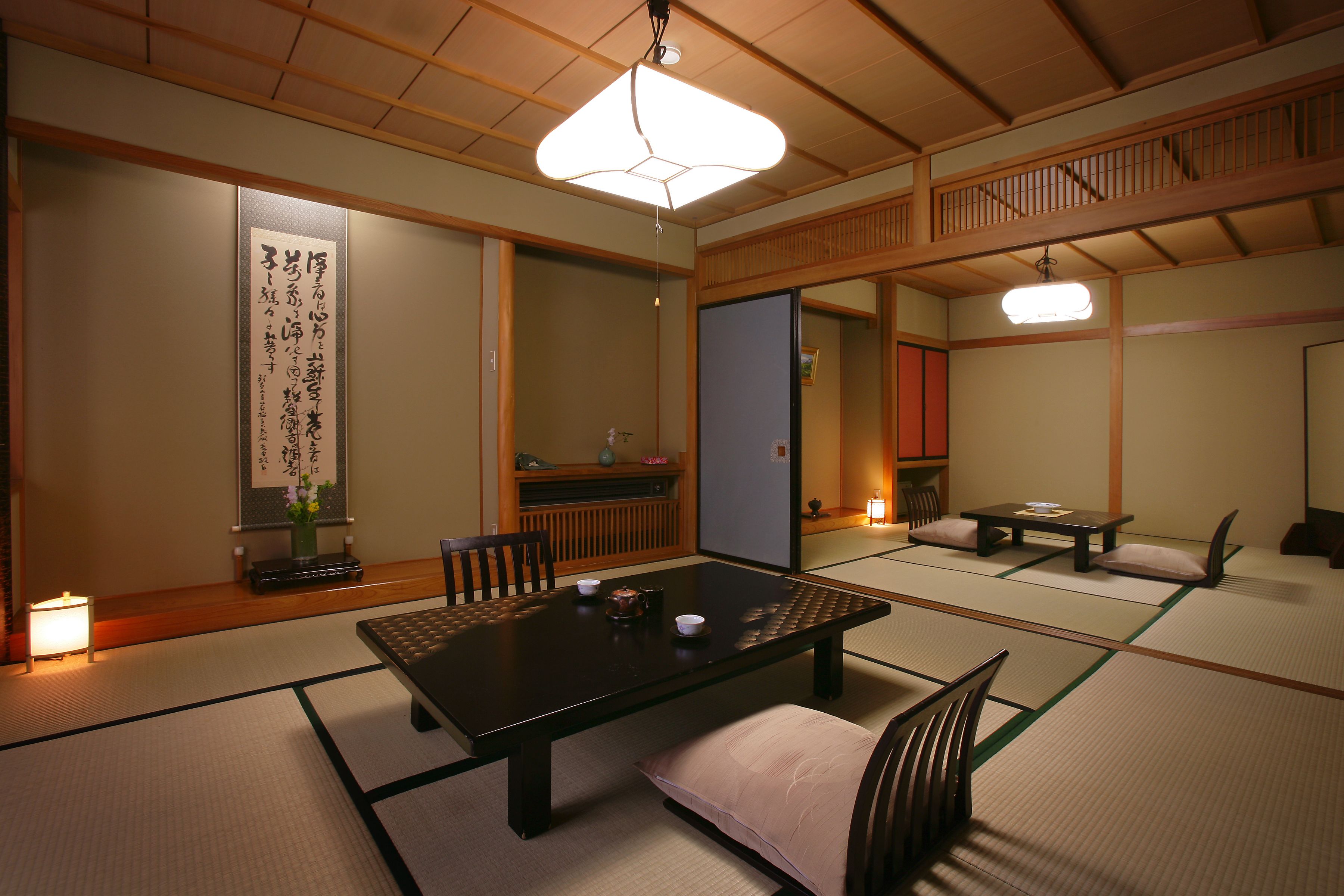 A traditional Japanese room with tatami flooring, a low table, and a hanging light fixture.