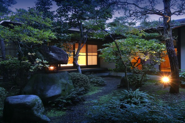 A traditional Japanese garden with a wooden building, large rocks, and a koi pond.