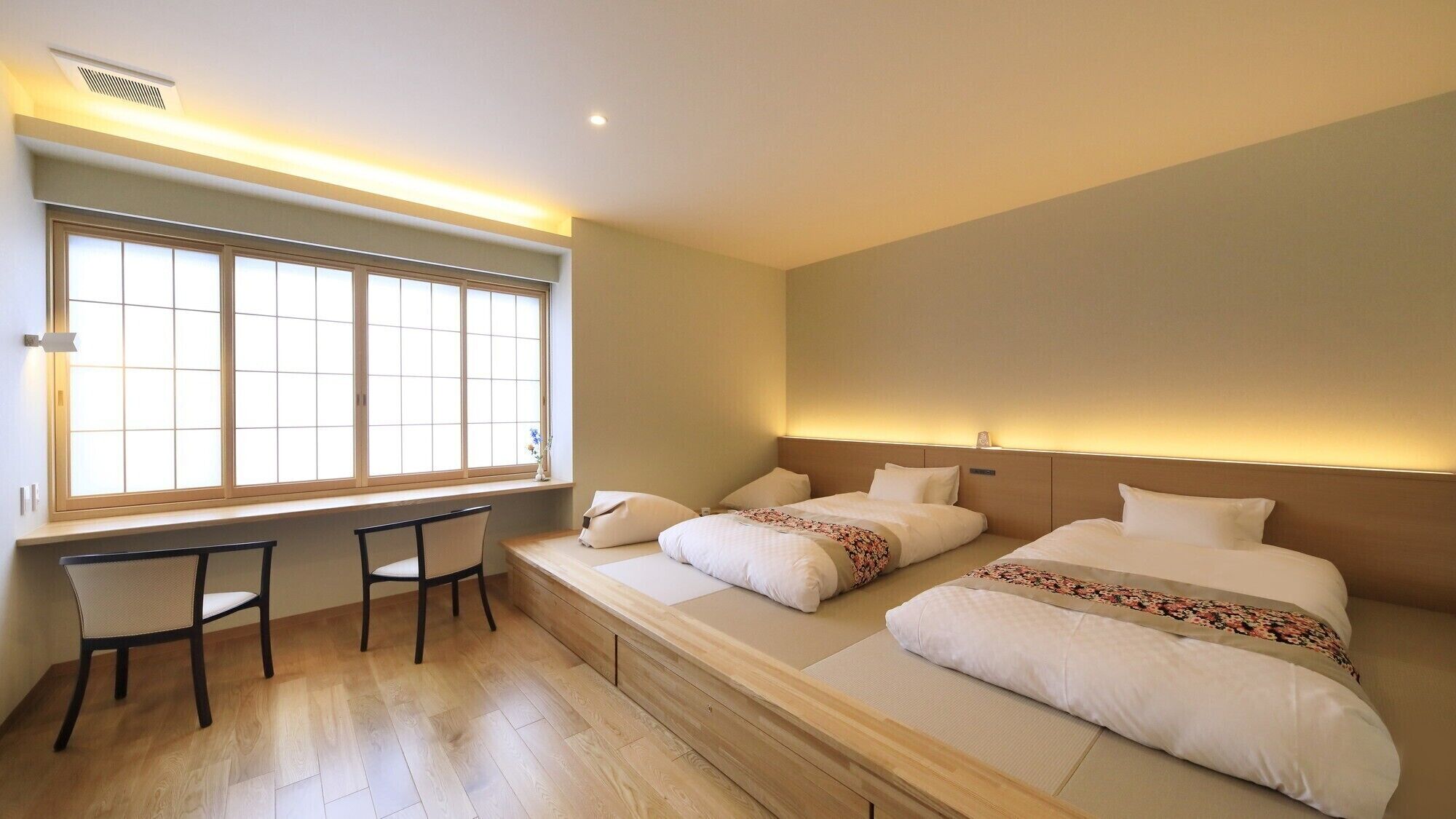 A hotel room with two beds, a desk, and a window with blinds.