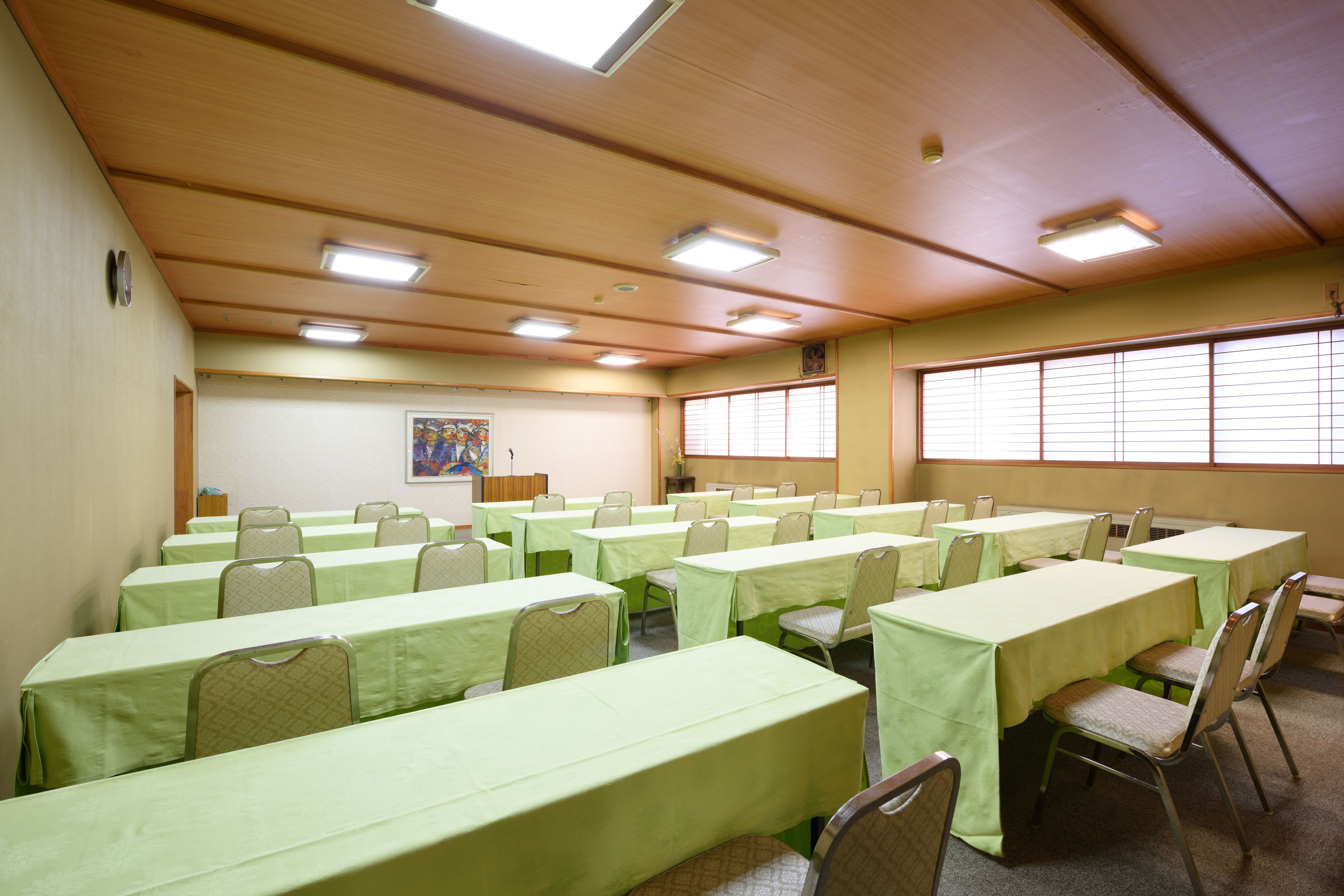 A conference room with multiple tables and chairs, wooden ceiling, and large windows.