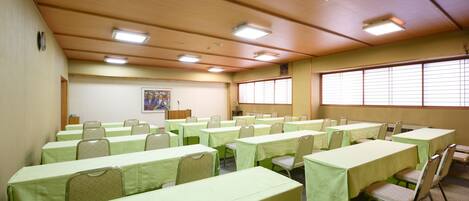 Un salón de conferencias con varias mesas y sillas, techo de madera y ventanas amplias.