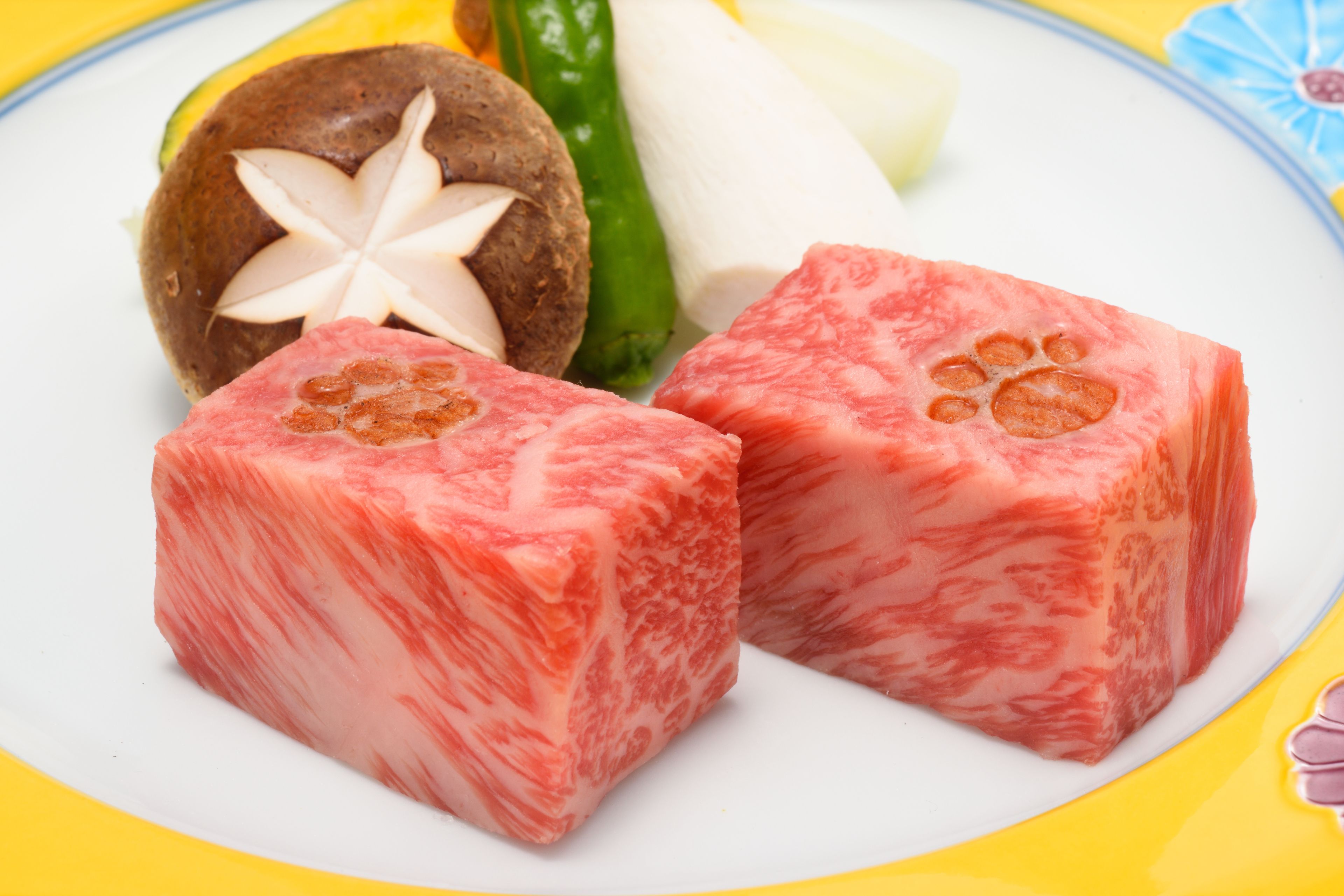 Dos trozos de carne rosada con centro blanco, un elemento marrón y redondo con una estrella blanca, y un chile verde sobre un plato.