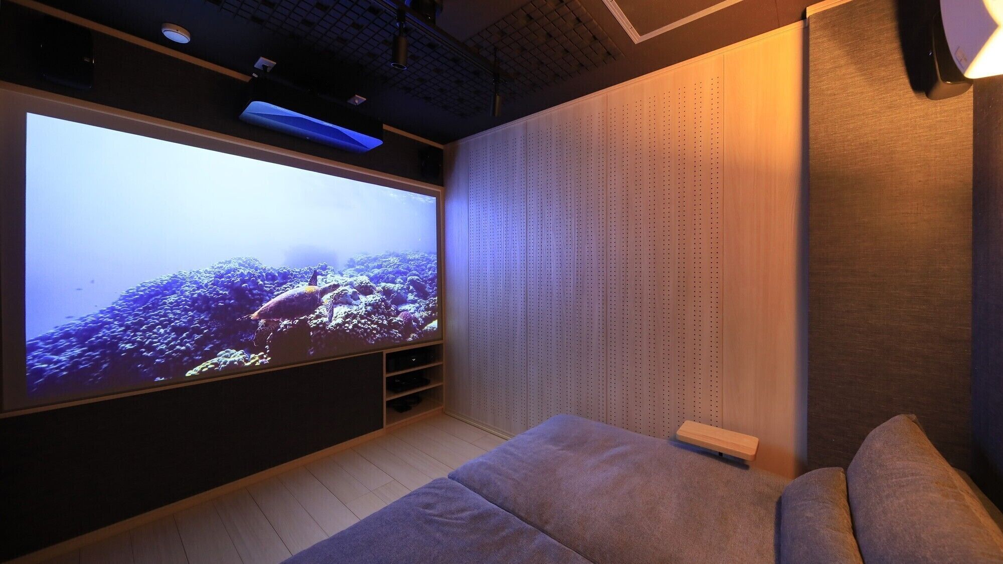 A room with a large flat-screen TV, a sofa, and a wall with a perforated design.