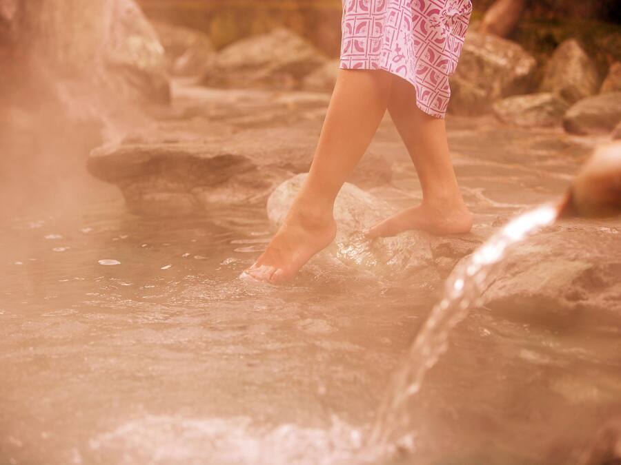 Eine Person geht barfuß in einer natürlichen Wasserlandschaft mit Steinen.
