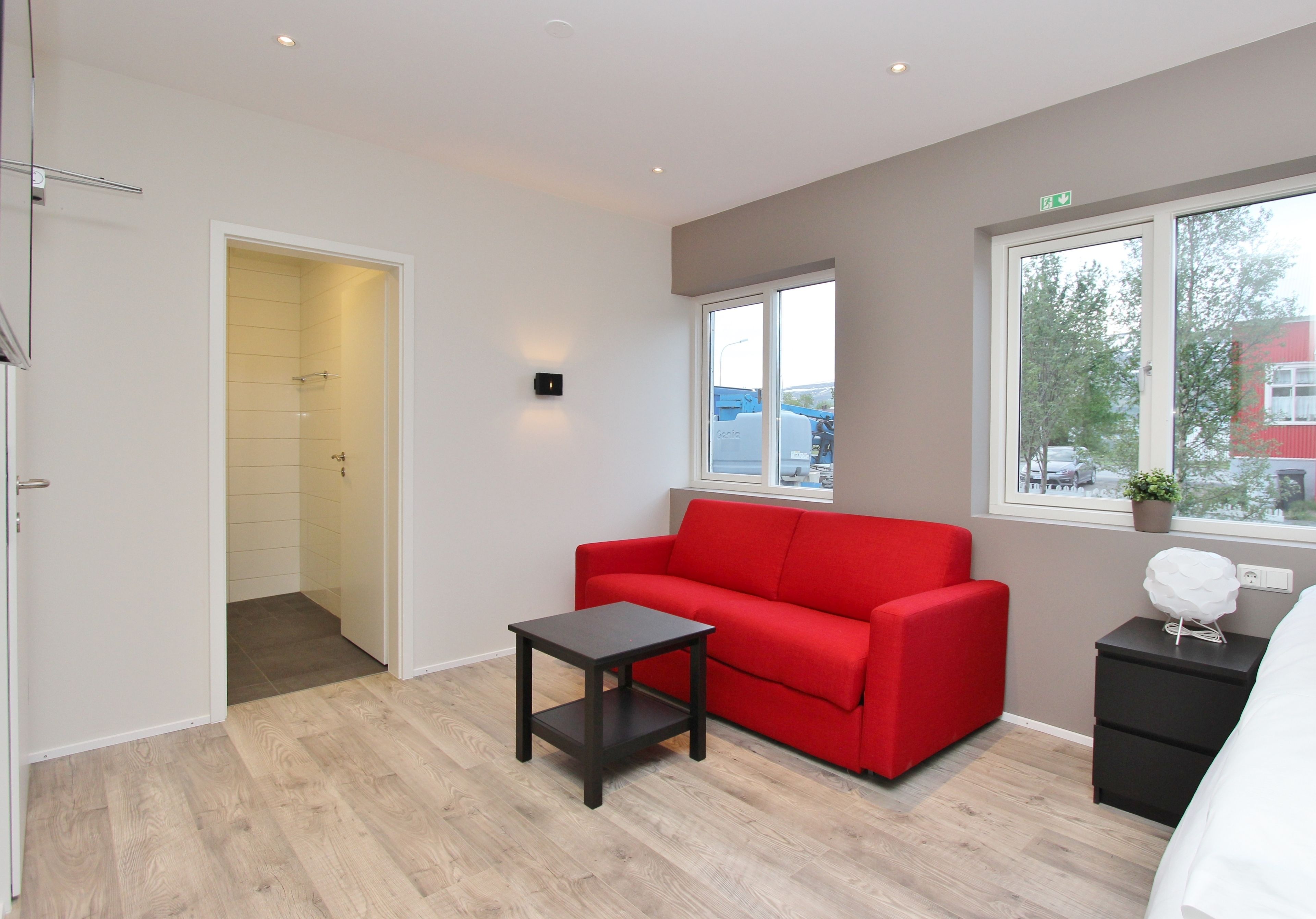 A modern room with a red sofa, a small table, a dresser, and a window with a view of the outside.