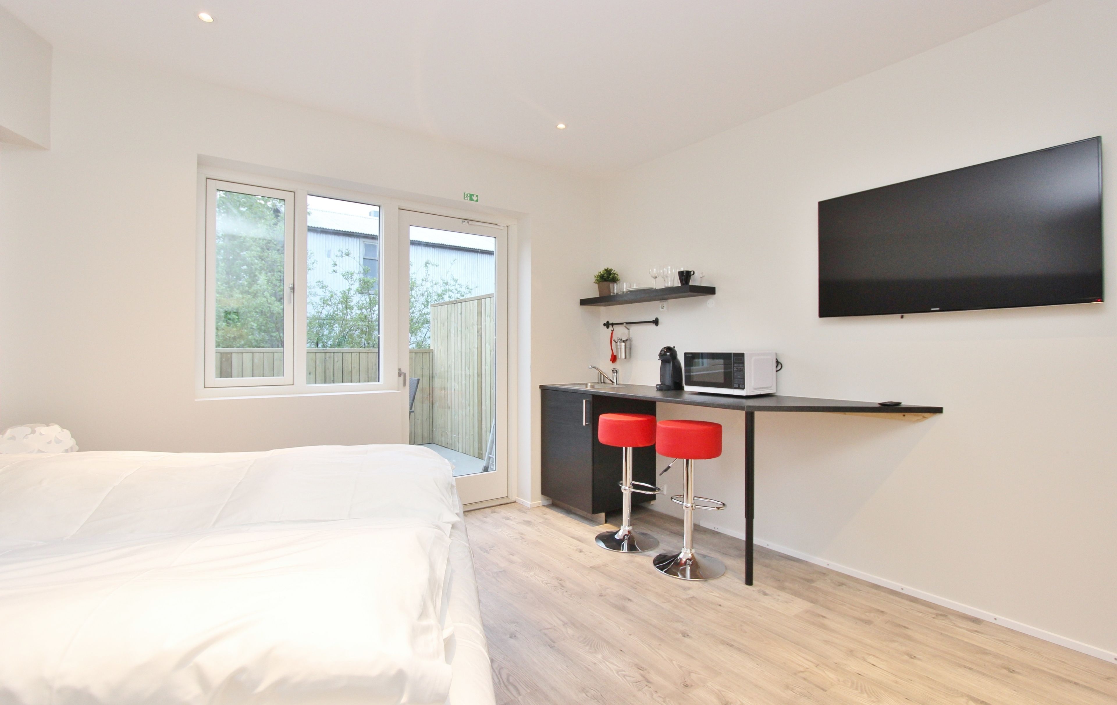 A modern bedroom with a bed, a small kitchenette, and a large window.