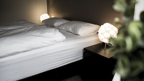 Un letto rifatto con lenzuola bianche e due lampade ai comodini dal design originale.