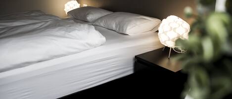 Una cama bien tendida con sábanas blancas y dos lámparas de noche de diseño singular.