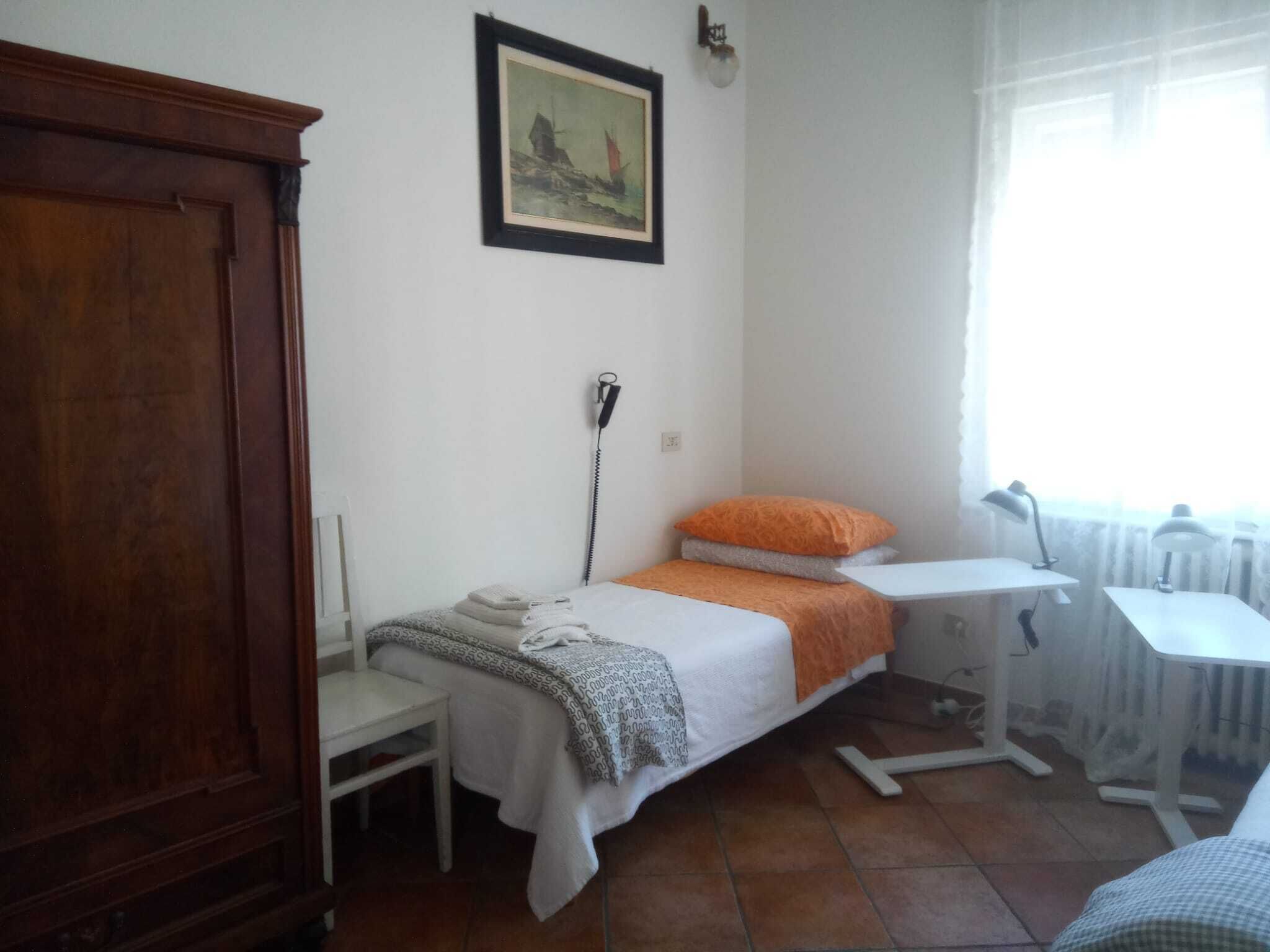 A bedroom with a bed, a desk, a chair, a radiator, and a wooden wardrobe.