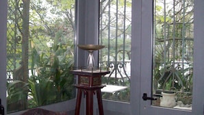 A conservatory with a chair, a table, and a view of greenery through ornate glass doors. - Villa Fiorita (Monfalcone)