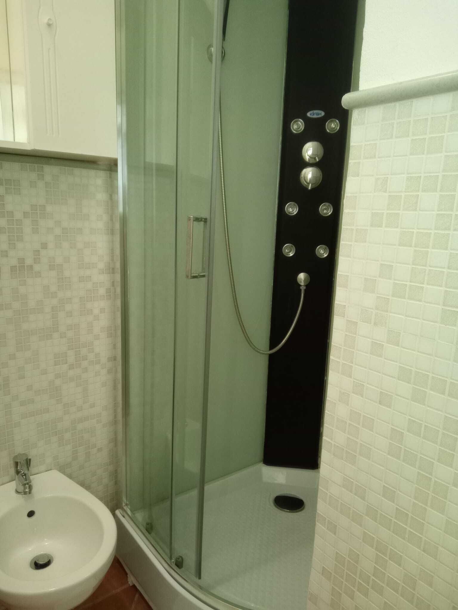 A bathroom with a glass-enclosed shower, a sink, and tiled walls.