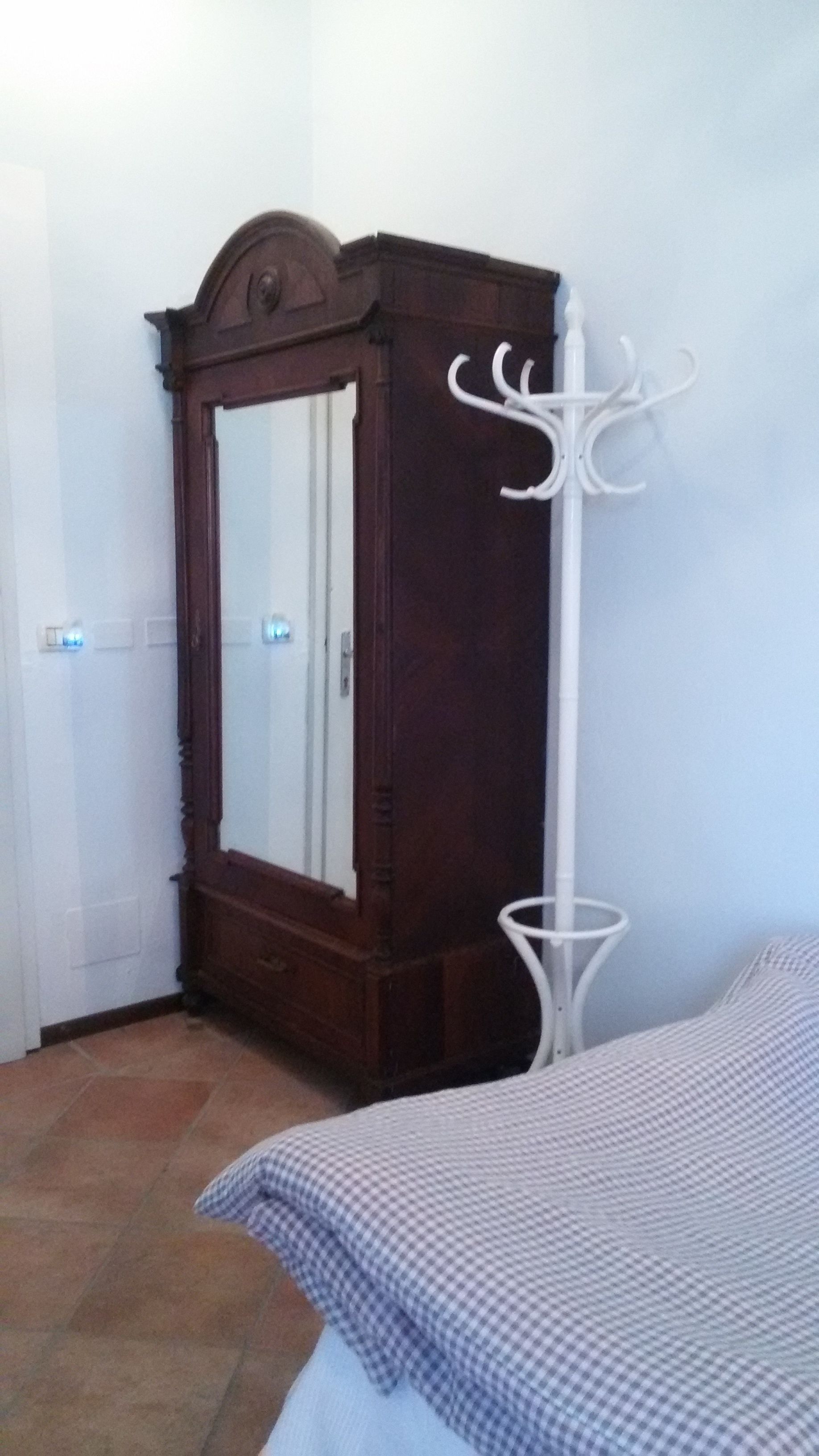 A bedroom with a wooden wardrobe, a white metal coat rack, and a checkered bedspread.