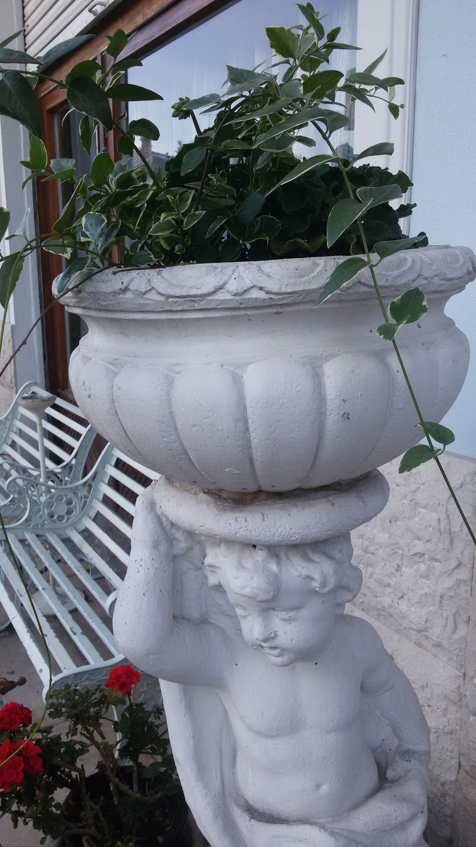 Un bac à fleurs en pierre blanche, orné d’une figurine décorative et contenant une plante.