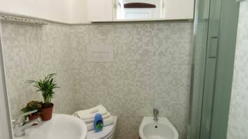 A bathroom with a sink, toilet, bidet, and a potted plant.