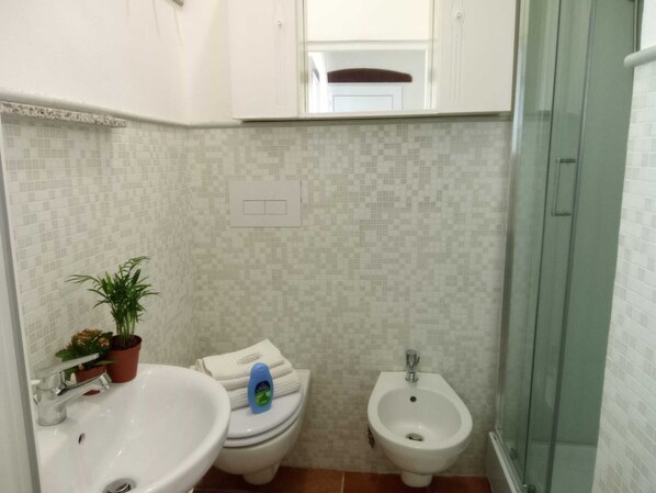 Un baño con lavamanos, inodoro, bidé y una planta en maceta.