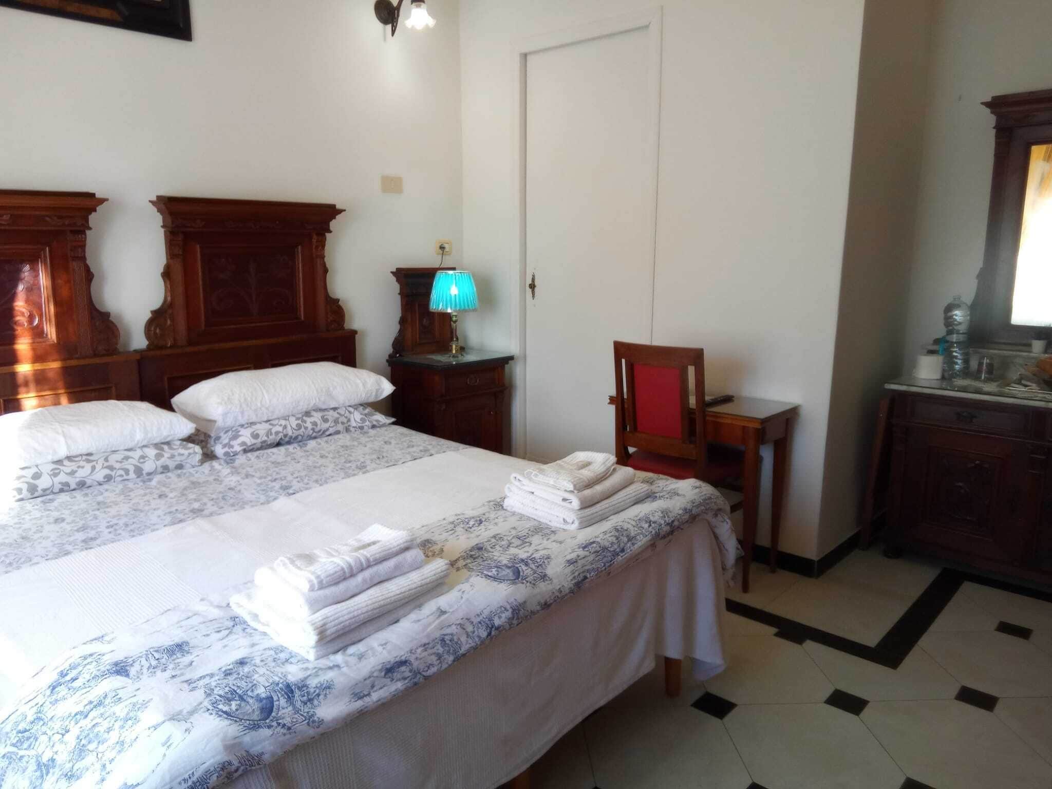 A hotel room with a large bed, a wooden dresser, a desk, and a chair.