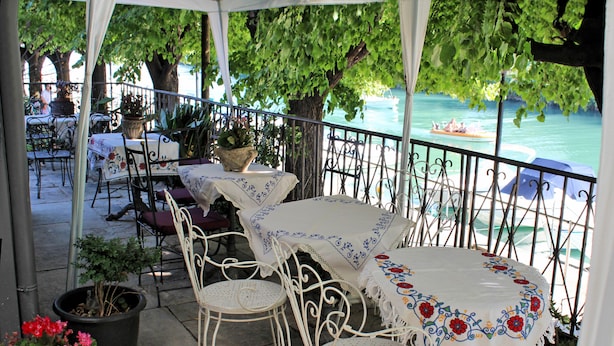 An outdoor patio with tables and chairs, surrounded by potted plants and overlooking a body of water with boats. - Villa Fiorita (Monfalcone)