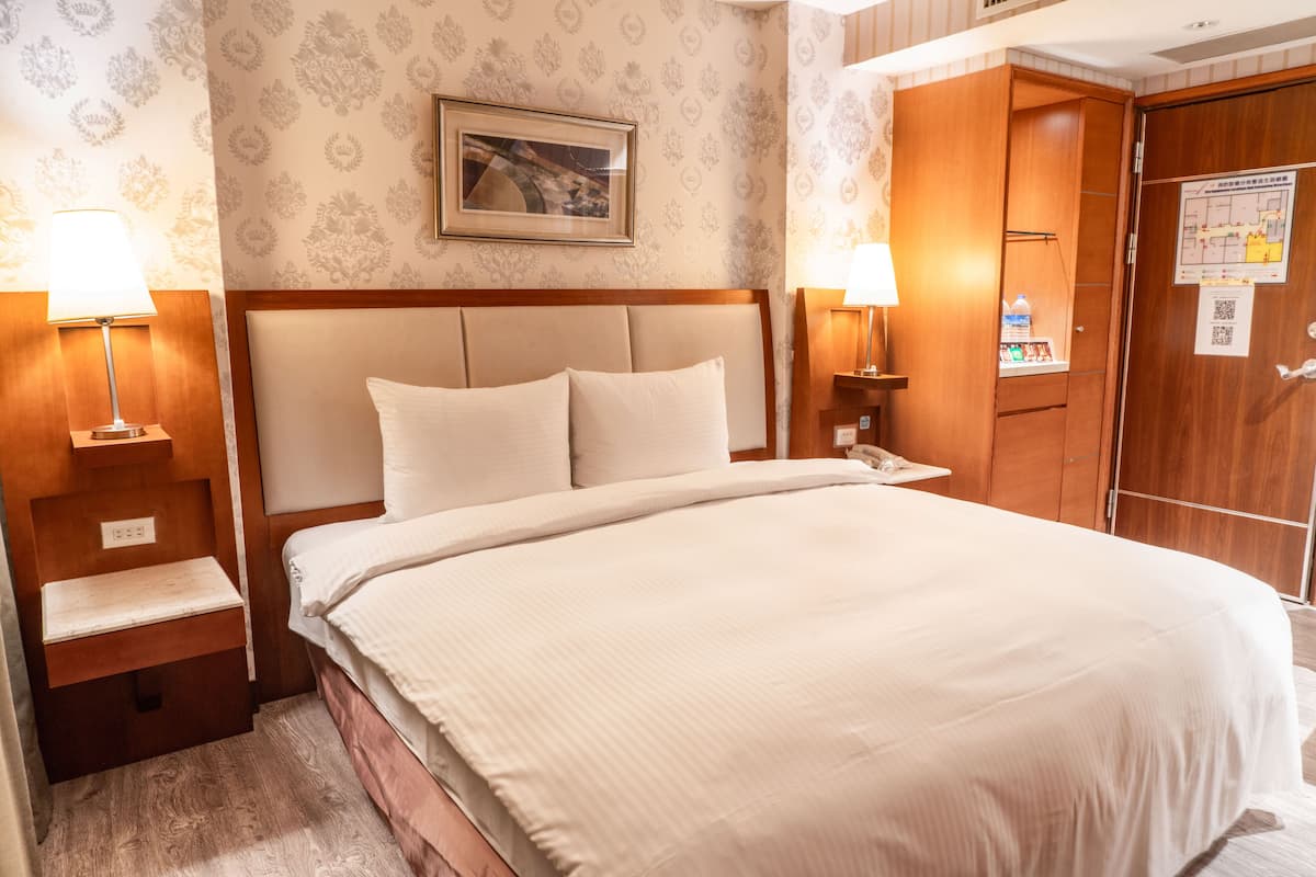 A neatly made bed with a headboard, two bedside tables with lamps, and a wooden wardrobe.