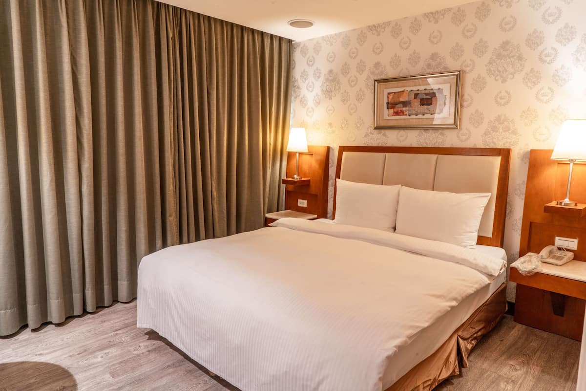 A hotel room with a large bed, two bedside tables with lamps, a framed picture on the wall, and a curtain on the window.