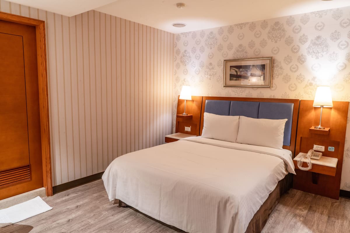 A hotel room with a large bed, wooden headboard, two bedside tables with lamps, a telephone, and a framed picture on the wall.