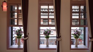 A hotel room with three windows, each with a curtain tied back, revealing a view of the street and buildings outside. - DG Hotel (Taipei)