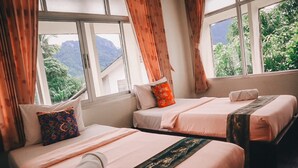 Een hotelkamer met twee bedden, elk voorzien van een kussen en een dekbed. De kamer heeft grote ramen met gordijnen en uitzicht op groen buiten.