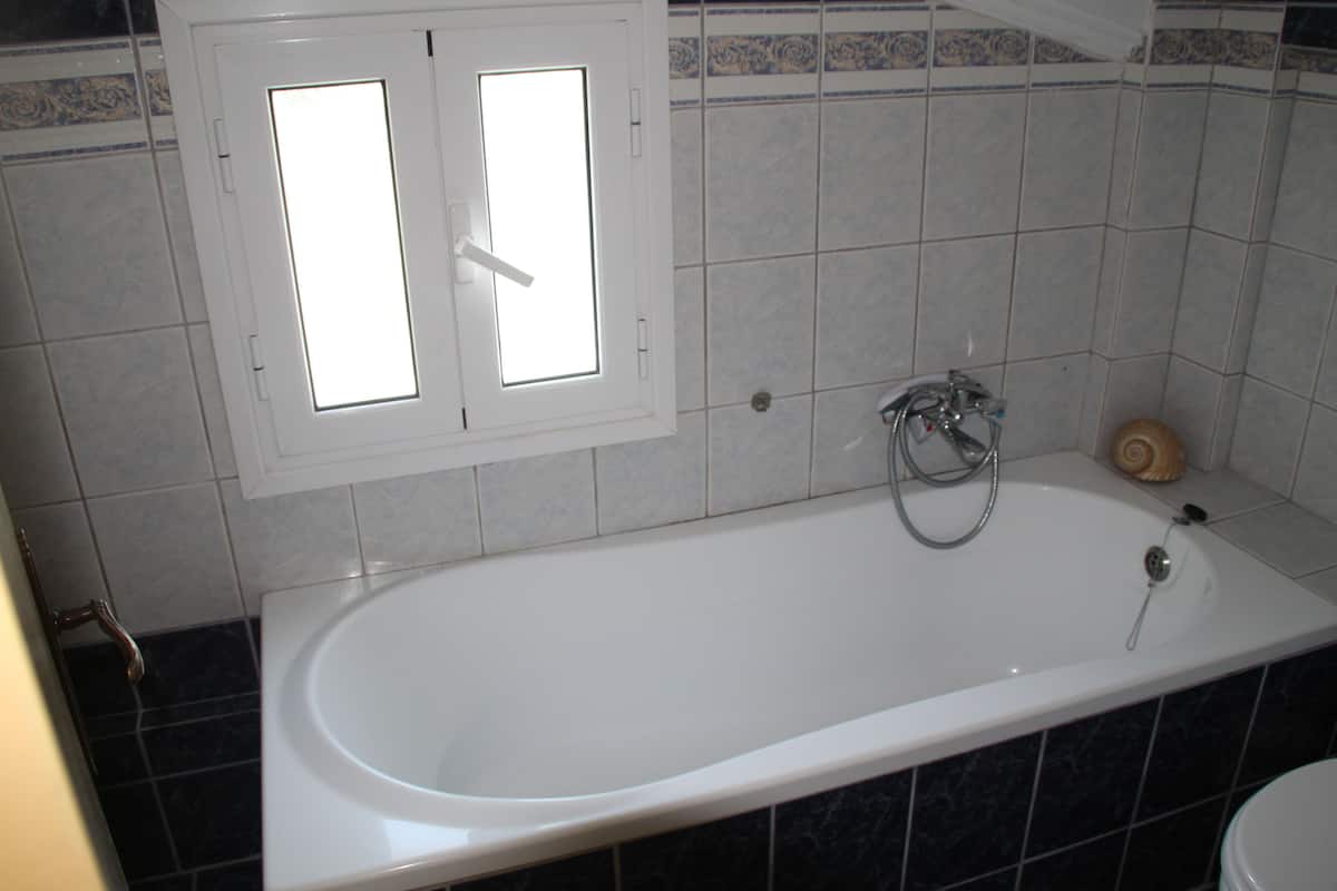 A bathroom with a bathtub, a window, and tiled walls.