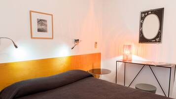 Een moderne hotelkamer met een houten hoofdeinde, een enkel bed, een klein rond tafeltje, een bureau met een spiegel en een ingelijst schilderij aan de muur.