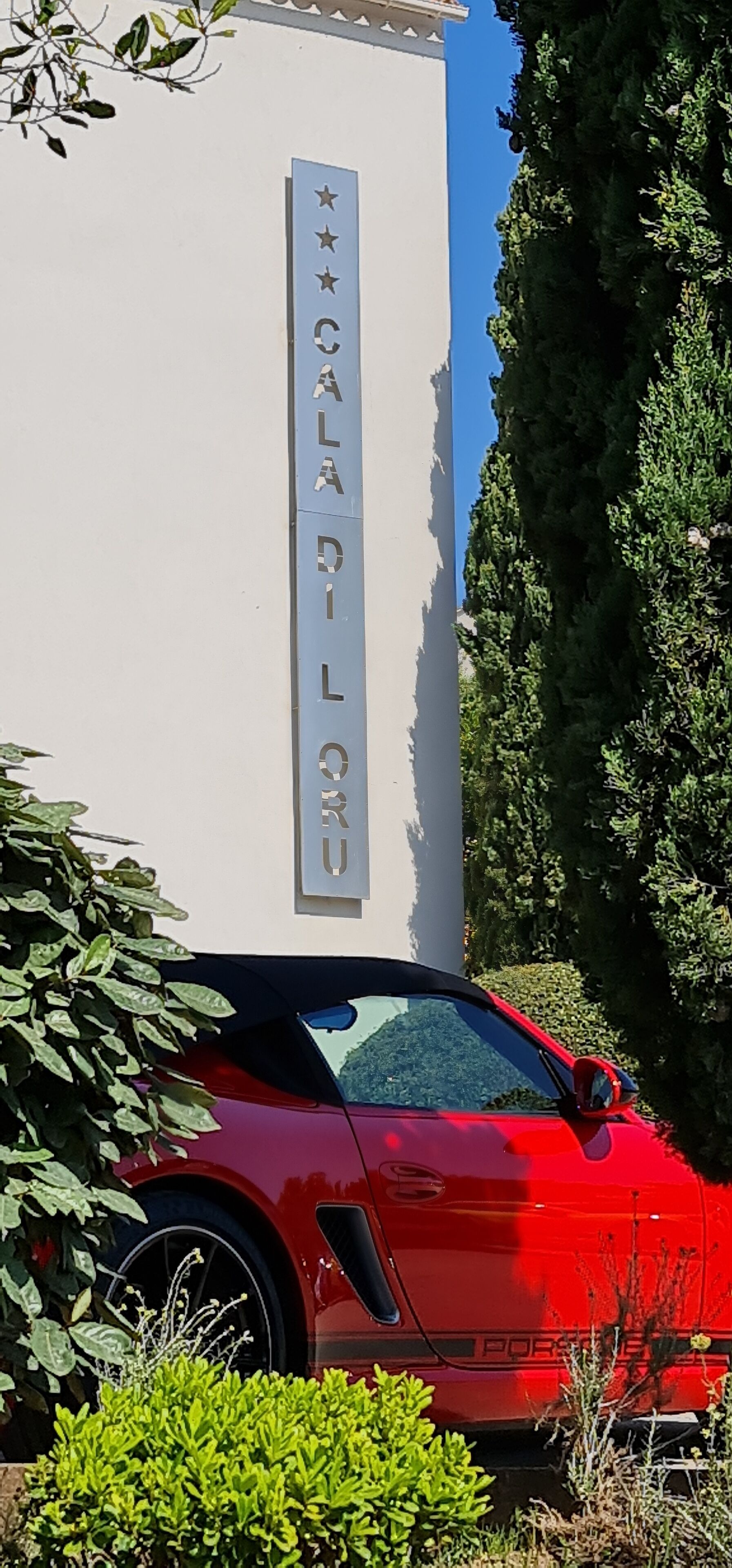 A red Porsche parked in front of a building with a sign reading "CALALU".