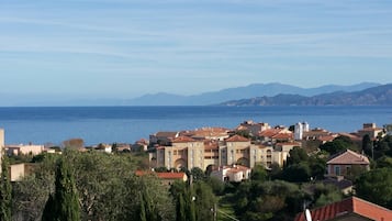 A coastal town with Mediterranean-style buildings, a sea view, and mountains in the background.