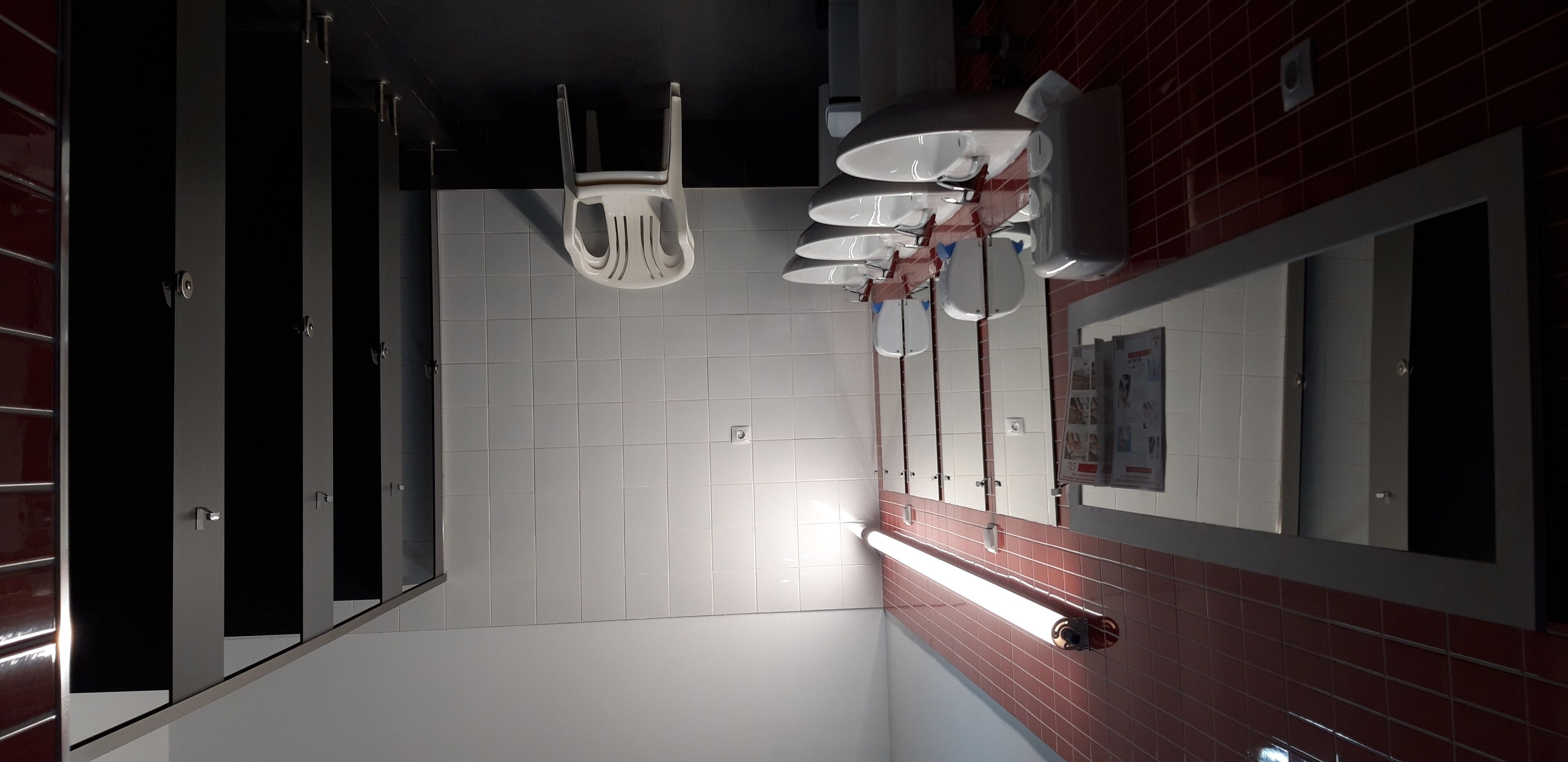 Un baño moderno con paredes de azulejos blancos, una pared de acento de ladrillo rojo y varios orinales.
