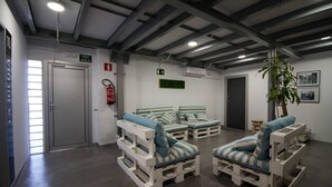 A room with white and blue striped lounge chairs, a green exit sign, and a fire extinguisher on the wall. - All Iron Hostel (Bilbao)